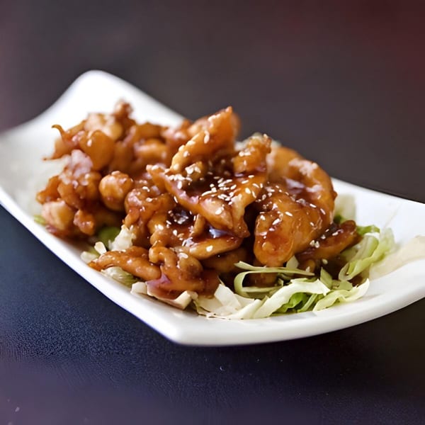 Lotus Xpress's sesame chicken, glistening with sauce and sprinkled with sesame seeds on a bed of lettuce.