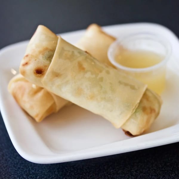 Two crispy egg rolls with a side of dipping sauce on a white plate from Lotus Xpress.