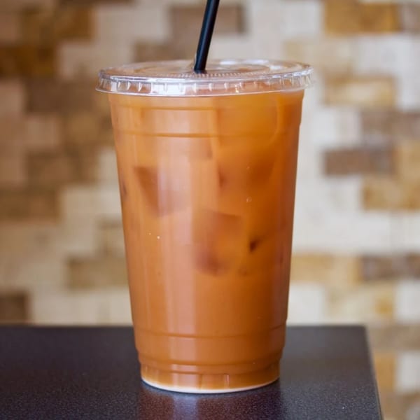 Iced Thai tea with a black straw in a clear plastic cup on a dark surface.