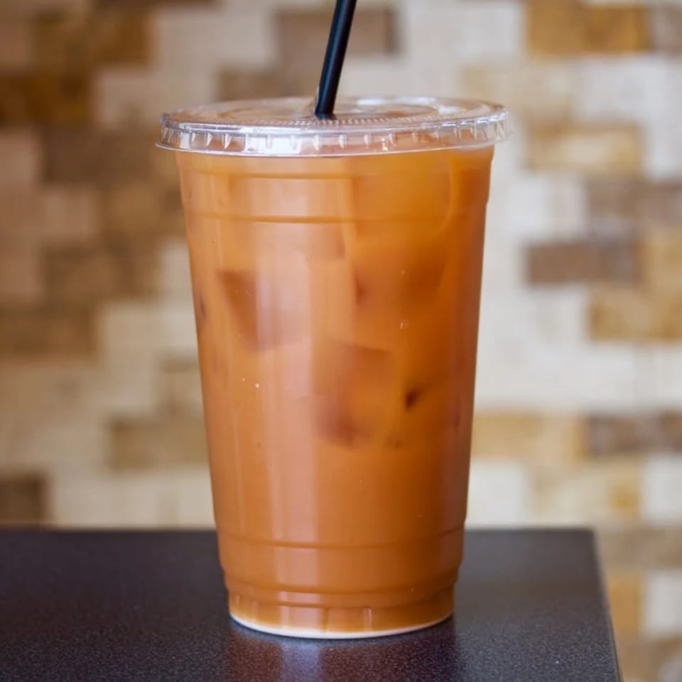 Iced Thai tea with a black straw in a clear plastic cup on a dark surface.
