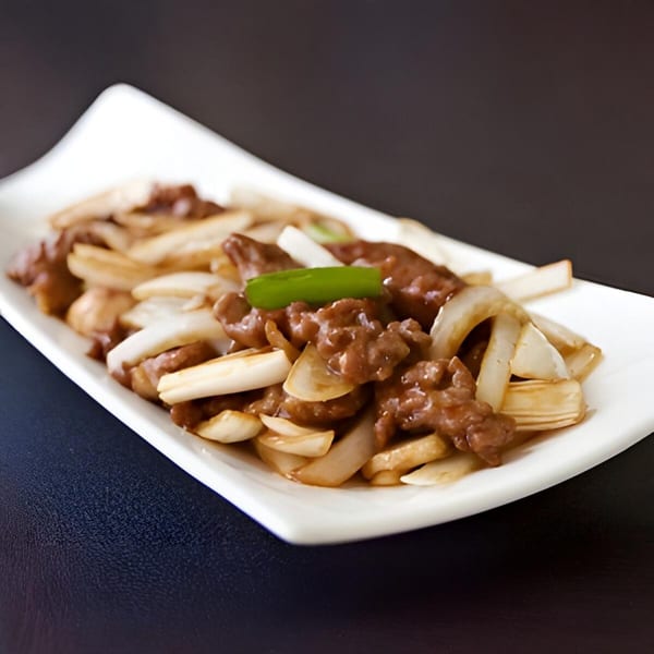 A white rectangular plate filled with beef and onions, garnished with a green pepper slice.